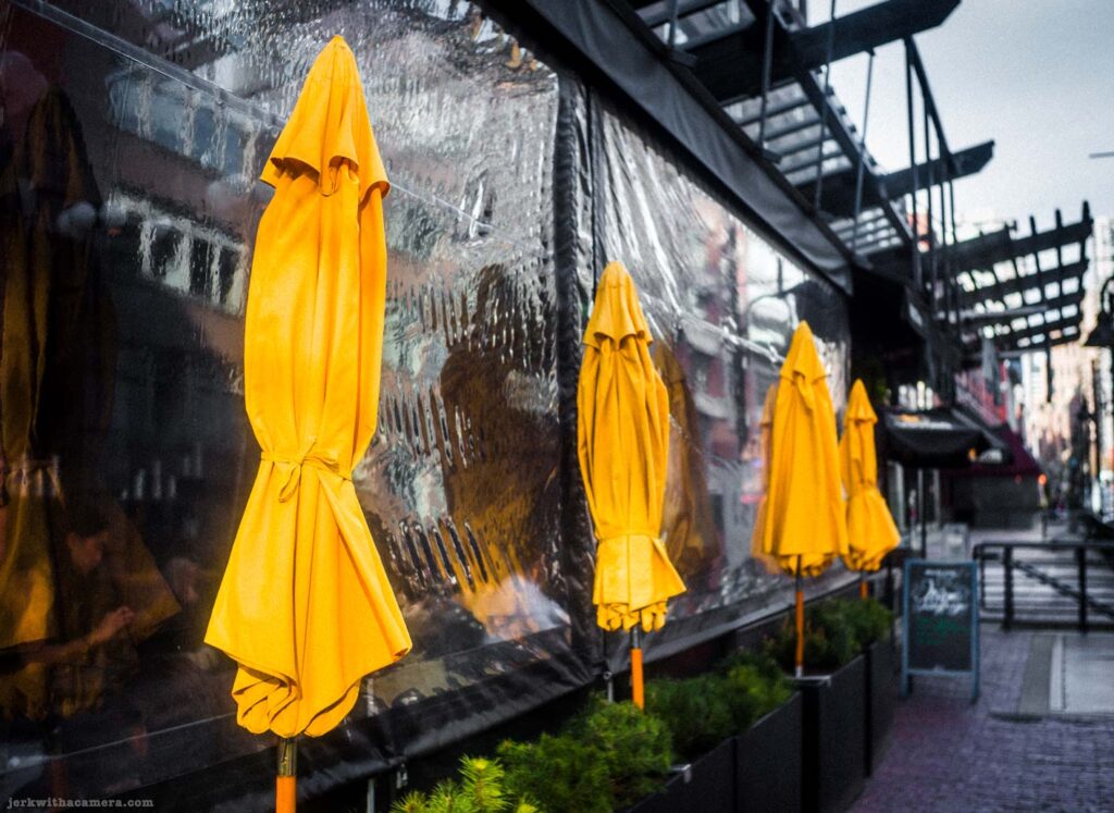 Closed yellow patio umbrellas beside outdoor restaurant seating area