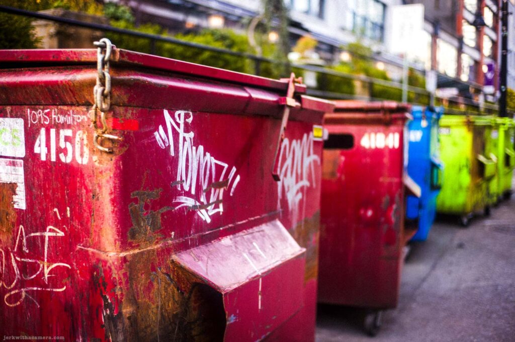 Red dumpsters with graffiti lined up in an alley