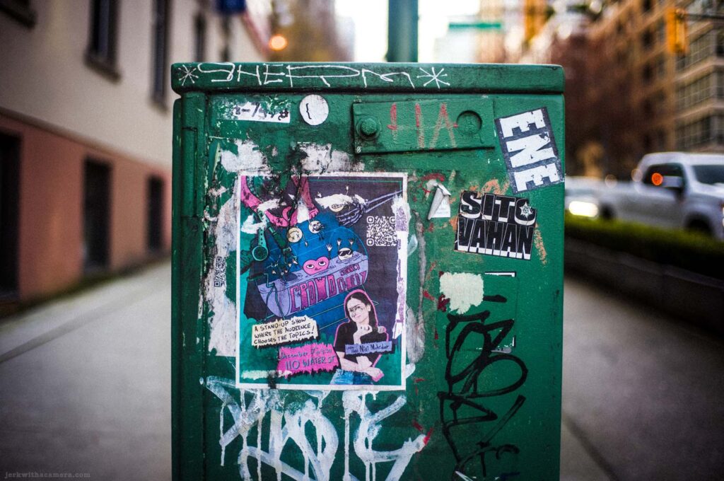 Green utility box covered in stickers graffiti and posters