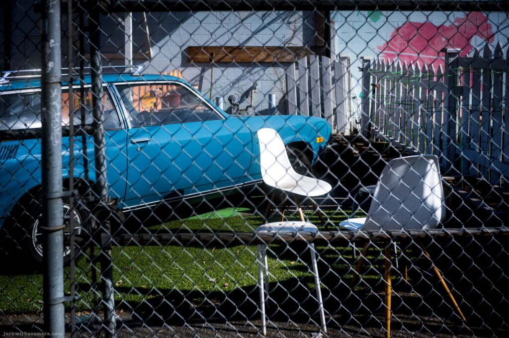 Blue car and white chairs behind a chain link fence