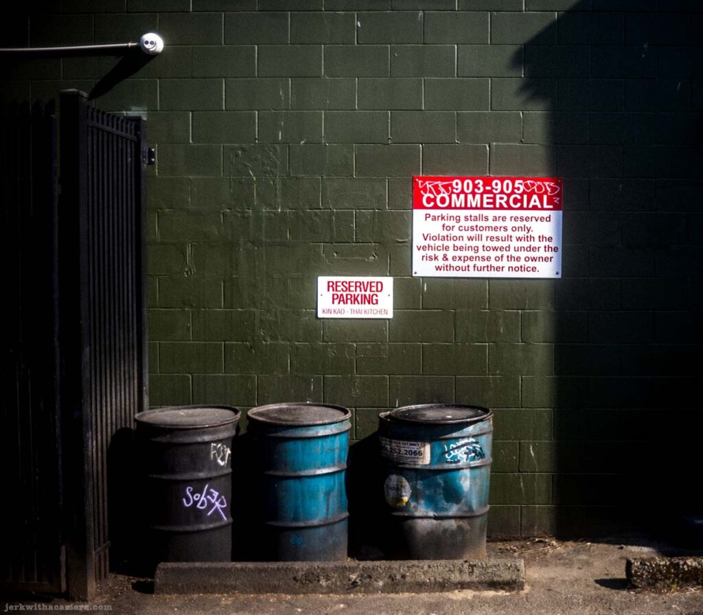 Parking sign above metal barrel against green brick wall on Commercial Drive in Vancouver
