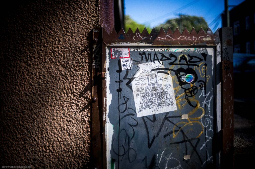 Graffiti-covered utility board with poster and sticker on Commercial Drive in Vancouver