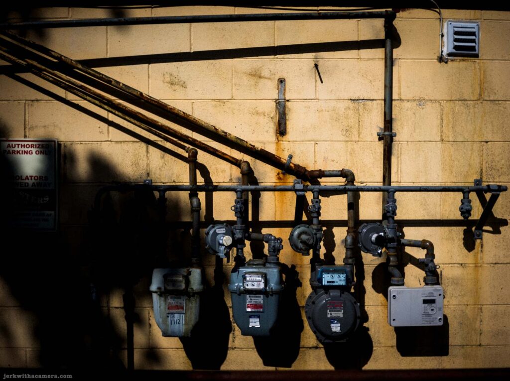 Gas meter and pipe mounted on concrete block wall with shadow on Commercial Drive in Vancouver