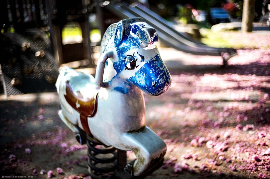 Playground spring rider horse with chipped paint beside slide on Commercial Drive in Vancouver
