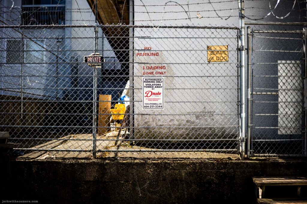 Chain-link fence with loading zone signs and barbed wire on Commercial Drive in Vancouver