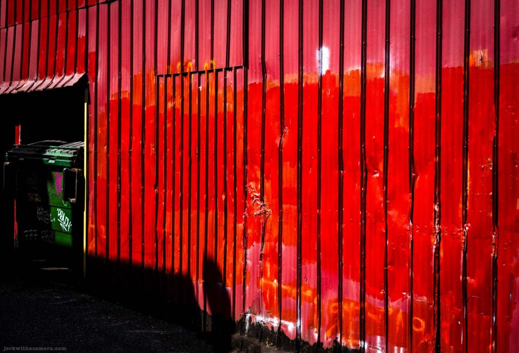 Red corrugated wall beside a green dumpster in an alley