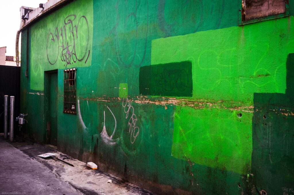 Green alley wall with graffiti and paint patches