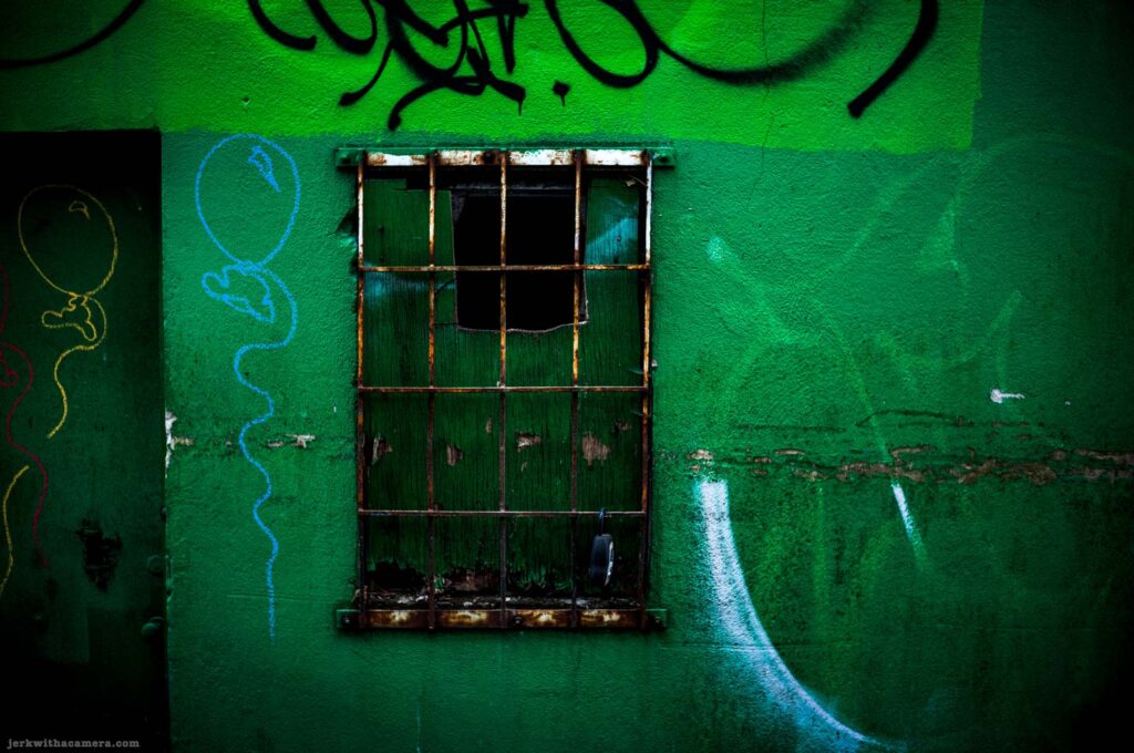Barred window on a green wall with graffiti
