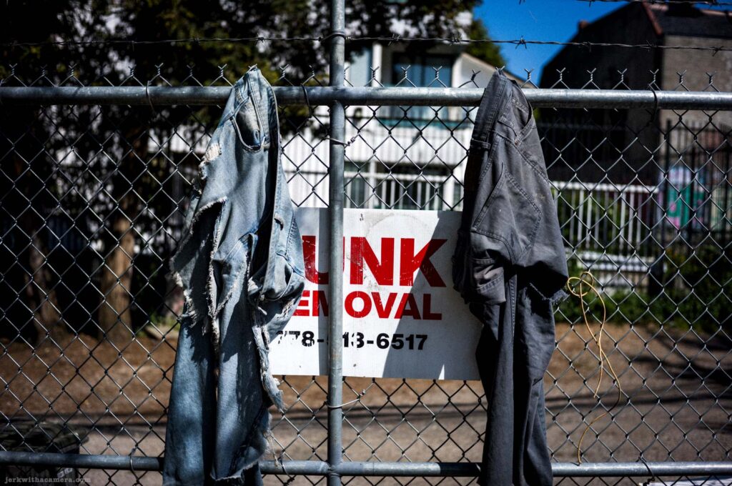 Jeans hanging on a chain link fence above a junk removal sign