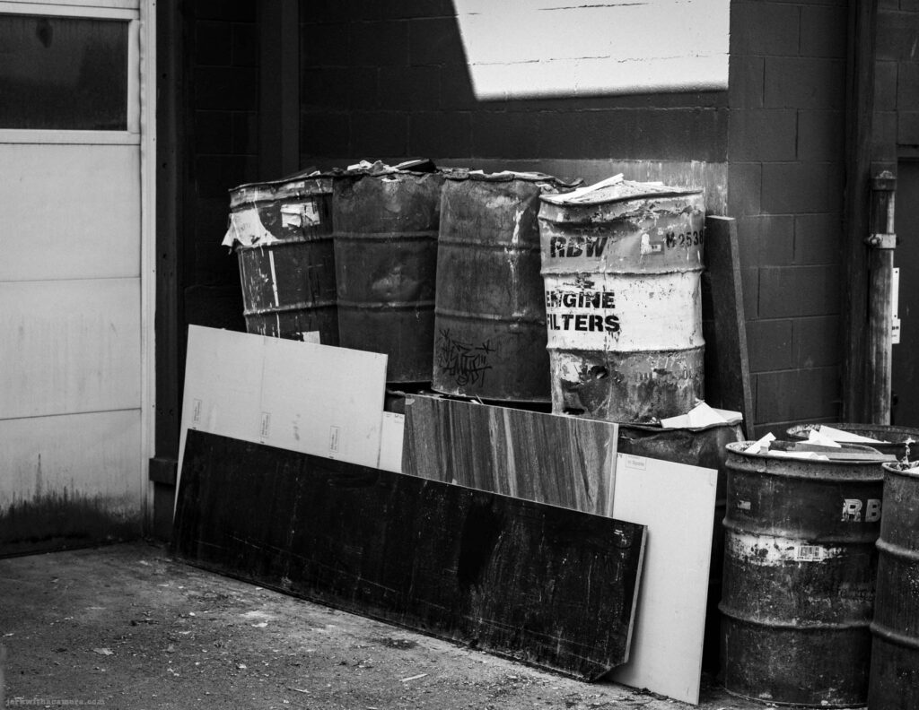 Metal barrels and boards stacked in an alley in black and white