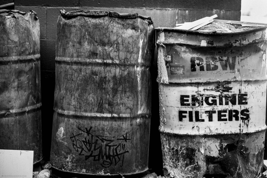 Engine filter barrel beside dented metal barrels in black and white