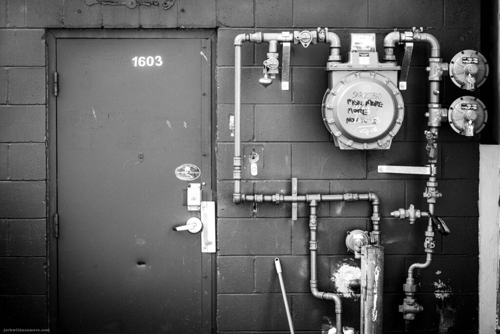 Metal door and gas meter mounted on black wall on Commercial Drive in Vancouver