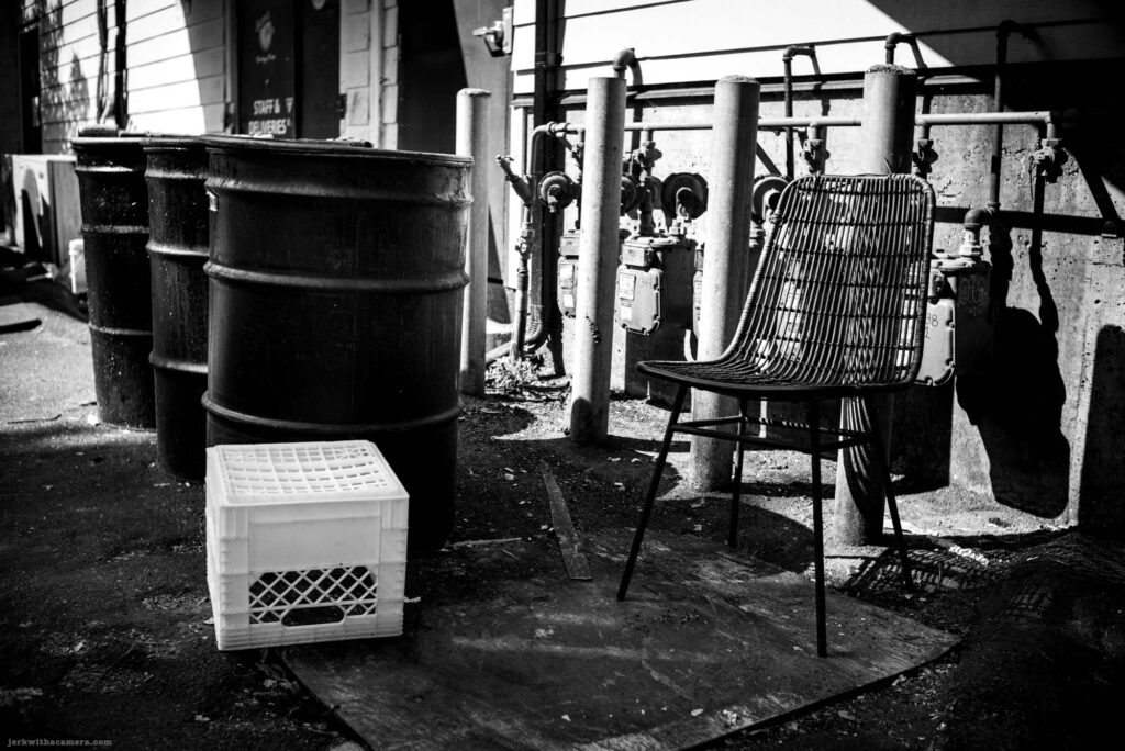 Chair beside metal barrel and utility meter on Commercial Drive in Vancouver