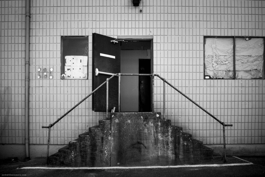 Concrete stair and open metal door on tiled wall on Commercial Drive in Vancouver