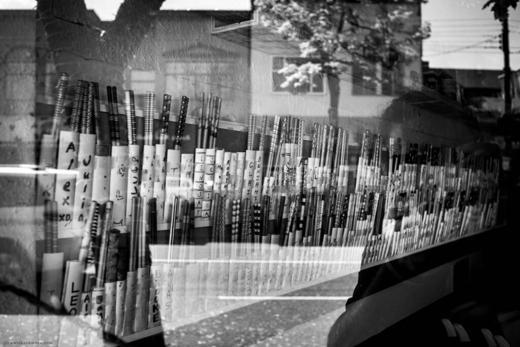 Rows of personalized chopsticks displayed behind window glass on Commercial Drive in Vancouver