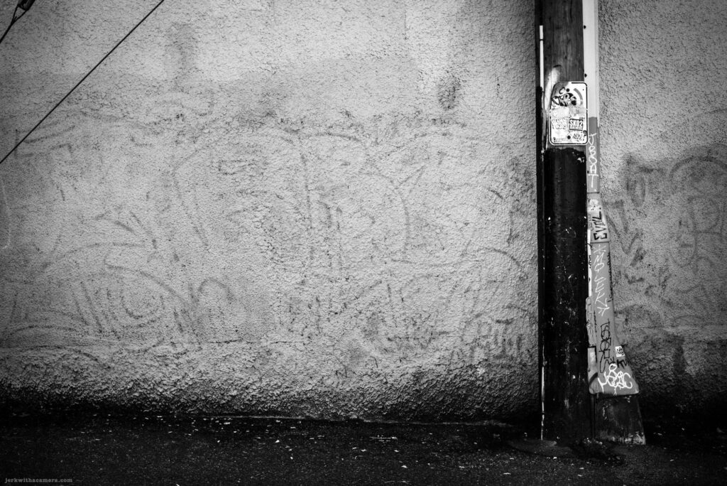 Utility pole with sticker and graffiti beside textured wall on Commercial Drive in Vancouver