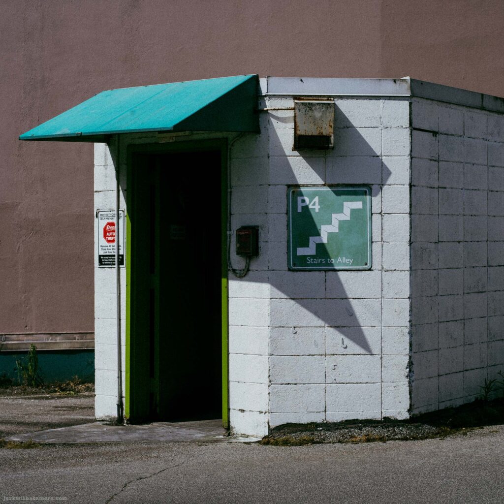 P4 stairwell entrance with teal awning and green door frame. Tighter framing than preceding frame. Pink stucco wall at right.