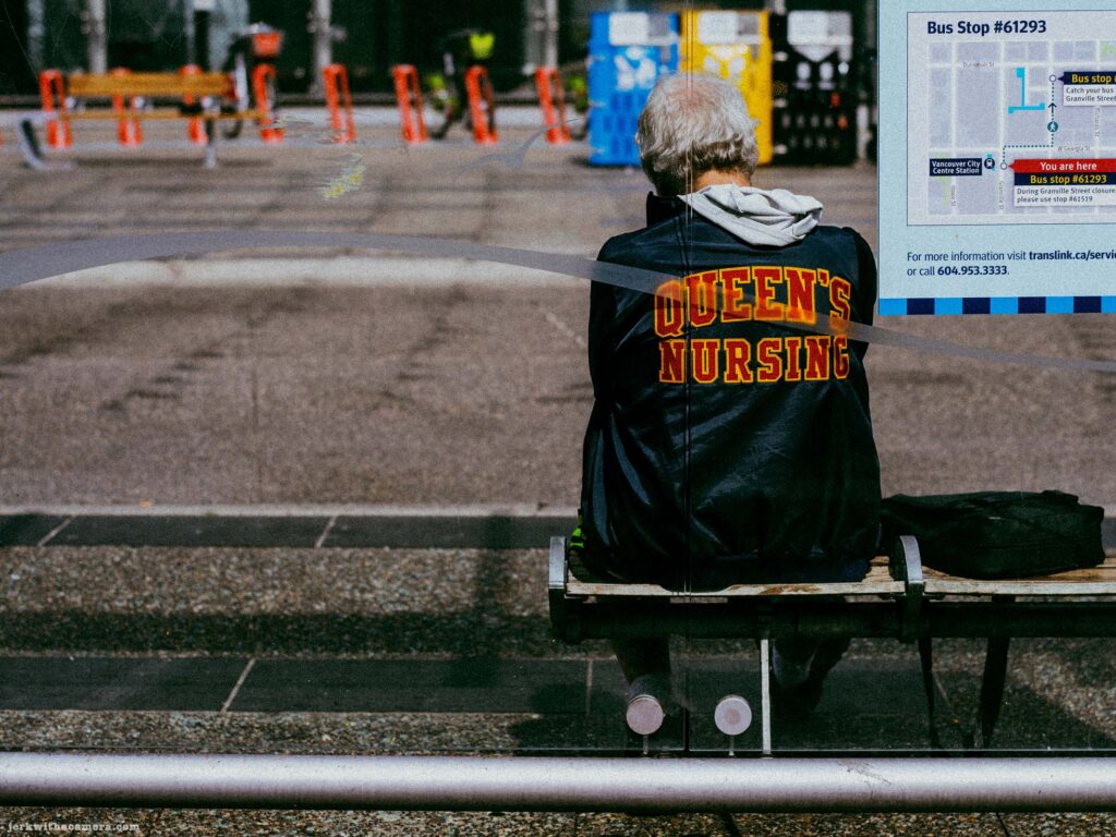 Person in Queen's Nursing jacket at bus stop. Granville Street Pedestrian Zone sign legible. Bus Stop 61293 noted on sign.