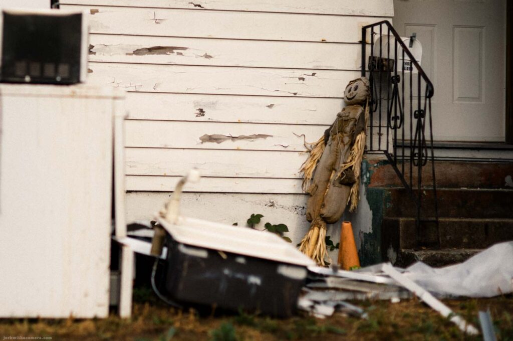 Discarded refrigerator and household items beside the entrance of a weathered house.